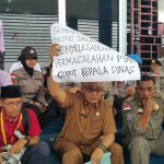 Kepala DPMPTSP Bintan, Hasfarizal Handra, memegang karton bertuliskan tuntutan mahasiswa yang menginginkan pencopotan dirinya sebagai kepala dinas saat aksi demo didepan Kantor DPMPTSP Bintan, Senin (30/12) siang. (okialexander/haluankepri.com)