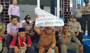 Kepala DPMPTSP Bintan, Hasfarizal Handra, memegang karton bertuliskan tuntutan mahasiswa yang menginginkan pencopotan dirinya sebagai kepala dinas saat aksi demo didepan Kantor DPMPTSP Bintan, Senin (30/12) siang. (okialexander/haluankepri.com)