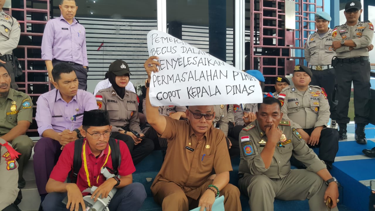 Kepala DPMPTSP Bintan, Hasfarizal Handra, memegang karton bertuliskan tuntutan mahasiswa yang menginginkan pencopotan dirinya sebagai kepala dinas saat aksi demo didepan Kantor DPMPTSP Bintan, Senin (30/12) siang. (okialexander/haluankepri.com)